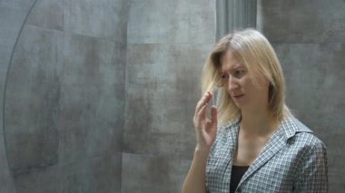 Genç sarışın kadın aynada saçının durumunu eleştirel olarak inceliyor. Yüzünde kaygı ve çekingenlik ifadesi var. Tatmin olmuyor..