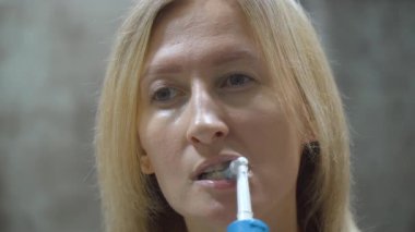 Sarışın kadın diş hijyeni rutinini gösteriyor, diş fırçasıyla dişlerini dikkatlice fırçalıyor, banyoda kişisel bakımını ön plana çıkarıyor.