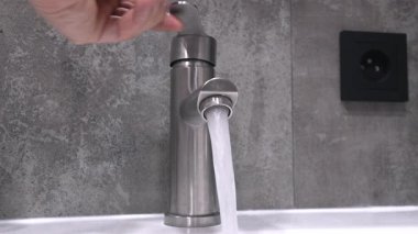 Profesyonel tesisatçı krom duş musluğunu manipüle ederek su basıncını ölçüyor. Ev bakımı sırasında modern gri kiremitli banyodaki akış dinamiklerini değerlendiriyor.