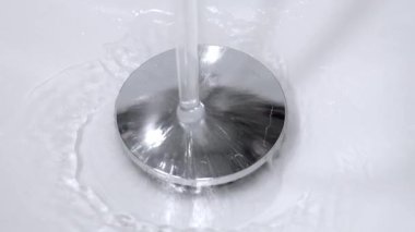 Su akıntısı el değmemiş beyaz lavabo lavabosundan aşağı akıyor, parlak krom dolgusu etrafında akıyor ve kademeli olarak seramik lavabonun içini dolduruyor.