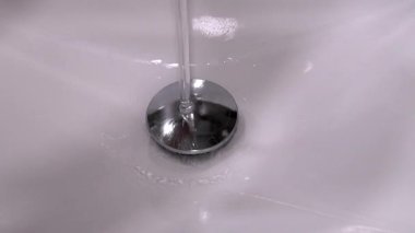Su akıntısı el değmemiş beyaz lavabo lavabosundan aşağı akıyor, parlak krom dolgusu etrafında akıyor ve kademeli olarak seramik lavabonun içini dolduruyor.