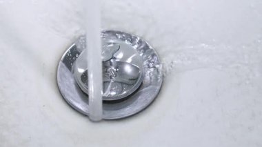 Su akıntısı el değmemiş beyaz lavabo lavabosundan aşağı akıyor, parlak krom dolgusu etrafında akıyor ve kademeli olarak seramik lavabonun içini dolduruyor.