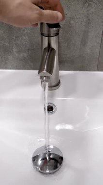 Profesyonel tesisatçı krom duş musluğunu manipüle ederek su basıncını ölçüyor, ev bakımı sırasında ev bakımı dikey video sırasında modern gri kartonlu banyodaki akış dinamiklerini değerlendiriyor.