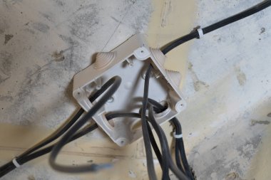 Kablolu elektrik bağlantı kutusu bina tadilatı sırasında beton bir tavana bağlanıyor, ev geliştirme ve elektrik işlerini temsil ediyor