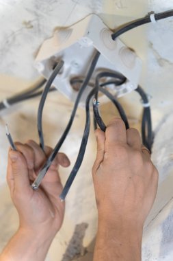 Elektrikçi elektrik tesisatı üzerinde çalışıyor, bir ev yenileme veya montaj projesi sırasında elektrik bağlantılarını bir bağlantı kutusuna dikkatlice bağlıyor. Dikey fotoğraf