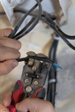 Elektrikçi, elektrik kablosundan yalıtım malzemelerini dikkatlice çıkarmak için kablo sökücüleri kullanıyor ve onu bir ev yenileme projesi sırasında bağlantı için hazırlıyor. Dikey fotoğraf