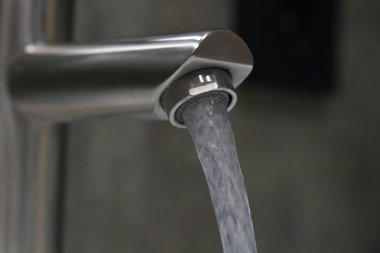 Temiz su akışı fırçalanmış nikel bir musluktan banyo lavabosuna akıyor, suyu koruma ve modern tesisat tesisatlarını vurguluyor.