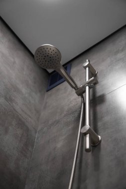 Modern duş başlığı çağdaş bir banyoda zarif bir şekilde asılı, zarif tasarımı ve işlevselliği vurguluyor gri fayansların şık zeminine karşı, boşluğun lüksünü ve rahatlığını artırıyor.