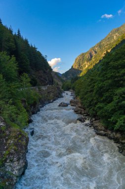 Beyazsu akıntıları, her iki tarafında yemyeşil ağaçlar ve kayalık uçurumlar olan dar bir geçitten geçerek, açık mavi bir gökyüzünün altında dramatik ve güçlü bir doğal manzara yaratır.