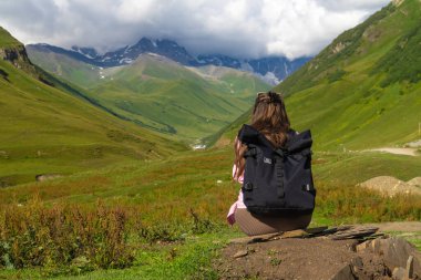 Sırt çantalı genç yürüyüşçü dinleniyor ve Gürcistan 'daki Kafkas dağlarının karlı tepelerinin manzarasının tadını çıkarıyor.