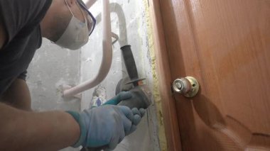 İnşaat işçisi, ahşap kapı çerçevesi yakınlarındaki beton duvar oluğunu dikkatlice keserek, önemli bir toz üretirken, profesyonel açı öğütücüsünü de yenileme projesi için kullanıyor.