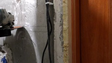 İnşaat işçisi, ahşap kapı çerçevesi yakınlarındaki beton duvar oluğunu dikkatlice keserek, önemli bir toz üretirken, profesyonel açı öğütücüsünü de yenileme projesi için kullanıyor.