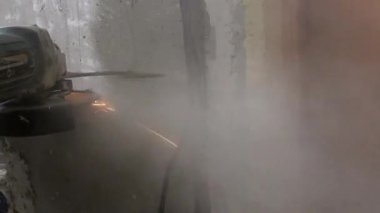 İnşaat işçisi, ahşap kapı çerçevesi yakınlarındaki beton duvar oluğunu dikkatlice keserek, önemli bir toz üretirken, profesyonel açı öğütücüsünü de yenileme projesi için kullanıyor.