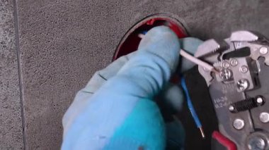 Koruyucu eldiven takan profesyonel elektrikçi elektrik kablolarını kabloyla dikkatlice söker ve bağlantı kutusunun içindeki bağlantıya hazırlar.