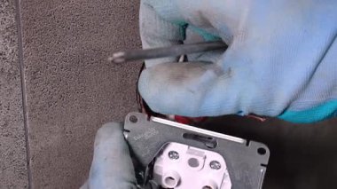 Koruyucu eldiven takan elektrikçi yeni elektrik prizini dikkatlice beton duvara yerleştirir, kabloları bağlar ve çıkış plakasını güvene alır