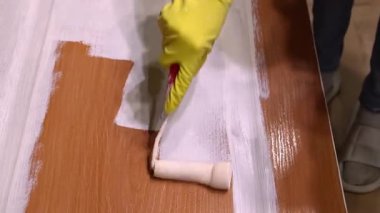 Becerikli bir ressam, ahşap kapıya paten kullanarak beyaz boya sürüyor. Ev yenileme projesi sırasında düzenli olarak üniforma kapsamı ve profesyonel kalitede iş görüyor.