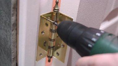 Marangozun ellerini dikkatlice beyaz kapıya elektrikli tornavida kullanarak altın menteşe yerleştirerek hassas yerleştirme ve güvenli bir şekilde tutturmayı sağlıyorlar. Vidalanmak ya da tahtaya kendi kendine dokunmak..