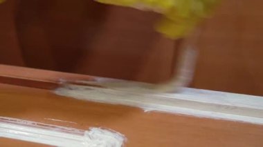 Sarı koruyucu eldivenler giyen yetenekli bir ressam ahşap kapı paneline beyaz boya sürüyor. Profesyonel ahşap işi tekniğini titizlikle ve titizlikle gösteriyor.