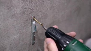 Profesyonel inşaat işçisi, iç mekâna mobilya monte etmeye hazırlanırken kablosuz matkabı kullanarak beton duvara metal destek yerleştiriyor.