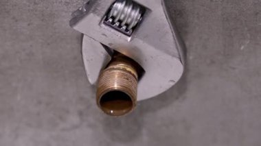 Profesyonel tesisatçı iç su sistemi bakımı sırasında ayarlanabilir ingiliz anahtarıyla pirinç boru tesisatını sıkıyor. Kesin bağlantı ve tamir aşamalarını gösteriyor.