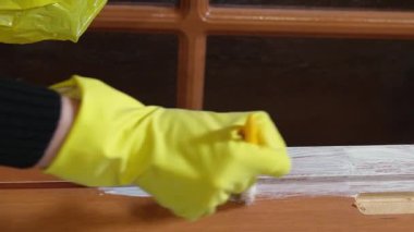 Deneyimli koruyucu eldiven giyen ressam, ahşap pencere çerçevesine veya kapıya dikkatlice beyaz boya sürerek, evi yenileme sürecinde yüzeyi dikkatlice dönüştürüyor.