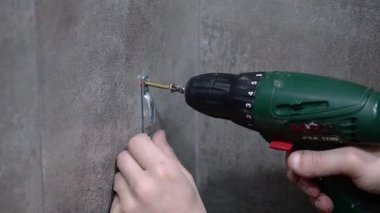 Profesyonel tamirci bosch psr 1200 kablosuz tornavida kullanarak vidaları sıkıyor, ev geliştirme projesi sırasında metalik kancayı gri kiremitli duvara güvenli bir şekilde takıyor