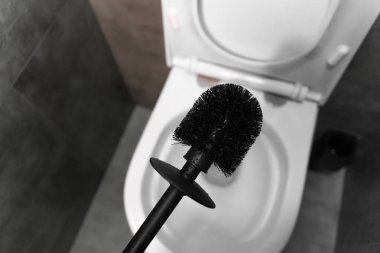 Modern siyah tuvalet fırçası açık beyaz bir klozetin üzerinde süzülüyor, modern bir banyoda temizliğe hazırlanıyor.