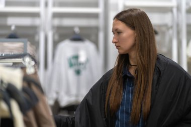 Kıyafet seçen, moda mağazasında alışveriş yapan, elbise rafının yanında duran, giysileri inceleyen, satın alma kararı veren şık bir kadın.