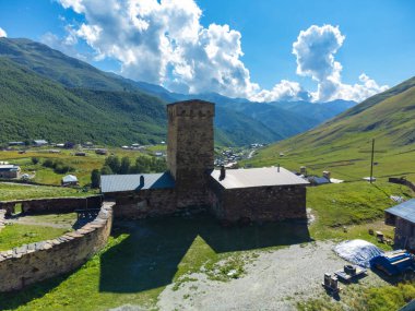Antik taş kule, güneşli bir günde beyaz bulutlarla arka planda yükselen Kafkasya dağları ile görkemli bir vadiye bakan, Gürcistan 'ın başkenti ushguli' de görkemli bir şekilde duruyor.