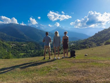 Üç turist, Gürcistan 'ın pitoresk manzaraları ve yürüyüş yolları ile tanınan ve güneşli bir günde doğanın güzelliğini alan Svaneti' de çarpıcı bir dağ manzarasının keyfini çıkarıyorlar.