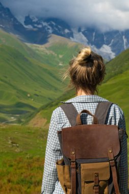 Sırt çantalı kadın yürüyüşçü, Gürcistan 'ın svaneti bölgesindeki kar kaplı dağların ve yeşil vadilerin çarpıcı manzarasının keyfini çıkararak doğanın güzelliğini ve macera ruhunu gözler önüne seriyor.