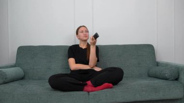 Genç kadın rahat bir şekilde kanepede oturdu, uzaktan kumandayla TV kanallarında gezindi, evinde boş zamanlarında oturma odasında dinlendi.