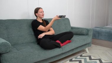 Genç kadın rahat bir şekilde kanepede oturdu, uzaktan kumandayla TV kanallarında gezindi, evinde boş zamanlarında oturma odasında dinlendi.