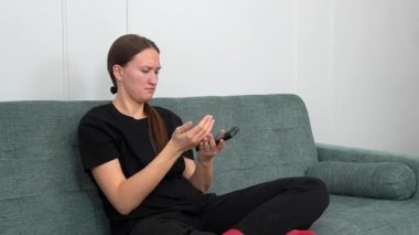 Genç kadın rahat bir şekilde kanepede oturdu, uzaktan kumandayla TV kanallarında gezindi, evinde boş zamanlarında oturma odasında dinlendi.