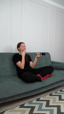 Genç bir kadın rahat bir koltukta oturup hayal kırıklığı yaşıyor. Hatalı TV uzaktan kumandasını sürekli düğmelere basarak ve kanalları dikey olarak değiştirerek kontrol etmeye çalışıyor.