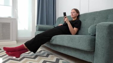 Genç kadın rahat bir şekilde kanepede oturdu, uzaktan kumandayla TV kanallarında gezindi, evinde boş zamanlarında oturma odasında dinlendi.