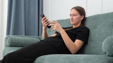 Genç kadın rahat bir şekilde kanepede oturdu, uzaktan kumandayla TV kanallarında gezindi, evinde boş zamanlarında oturma odasında dinlendi.