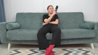 Genç kadın rahat bir şekilde kanepede oturdu, uzaktan kumandayla TV kanallarında gezindi, evinde boş zamanlarında oturma odasında dinlendi.