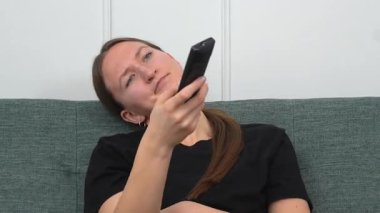 Genç kadın rahat bir şekilde kanepede oturdu, uzaktan kumandayla TV kanallarında gezindi, evinde boş zamanlarında oturma odasında dinlendi.