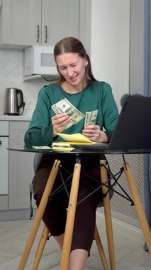 Genç, profesyonel bir kadın kişisel mali durumunu analiz ediyor, bütçeyi yönetiyor, nakit sayıyor, modern mutfak ortamında çalışırken dizüstü bilgisayarına detaylı notlar alıyor. Dikey video