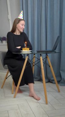 Parti başlıklı genç kadın online doğum gününü kutluyor, dizüstü bilgisayar kullanıyor, ekrana bakıyor, elinde pasta ve mum ile tabağı tutuyor, gülümsüyor ve uzaktan ailesiyle konuşuyor.