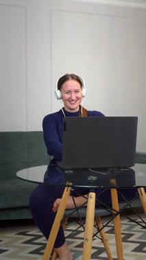 Kulaklık takan, video görüşmesi yapan, uzaktan çalışma sırasında rahat bir şekilde koltukta oturan, laptopla odaklanmış ifadeyle iletişim kuran genç bir profesyonel. Dikey video