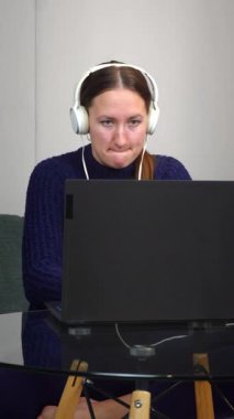 Video konferansına katılan profesyonel iş kadını, ev ofisinden bilgisayarla uzaktan çalışıyor, kulaklık takıyor ve çevrimiçi iş görüşmeleri sırasında dikey görüntülere odaklanıyor.