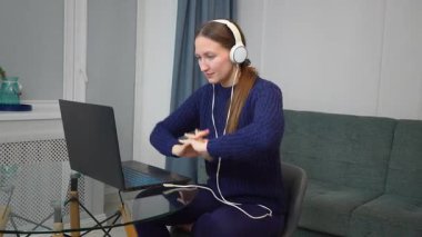 Video konferansına katılan profesyonel iş kadını, ev ofisinden bilgisayarla uzaktan çalışıyor, kulaklık takıyor ve çevrimiçi iş toplantısı sırasında dikkatle odaklanıyor.