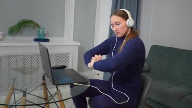 Kulaklık takan, dizüstü bilgisayar kullanan ve masada otururken müzik dinleyen genç bir oyuncu. Gülümseyen öğrenci ve günlük giysiler kablosuz teknoloji ve bilim podcast dinleyerek online çalışıyor.