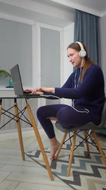 Kulaklık takan, dizüstü bilgisayar kullanan ve masada otururken müzik dinleyen genç bir oyuncu. Gülümseyen öğrenci ve günlük giysiler kablosuz teknoloji ve bilim podcast dinleyerek online çalışıyor.