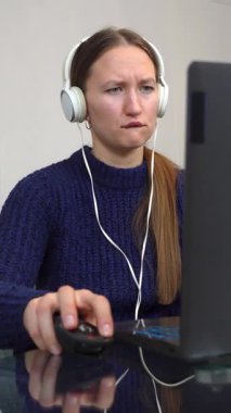 Kulaklık takan, dizüstü bilgisayar kullanan ve masada otururken müzik dinleyen genç bir oyuncu. Gülümseyen öğrenci ve günlük giysiler kablosuz teknoloji ve bilim podcast dinleyerek online çalışıyor.