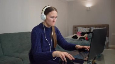 Kulaklık takan, dizüstü bilgisayar kullanan ve masada otururken müzik dinleyen bir bayan oyuncu. Gülümseyen Öğrenci ve Gelişigüzel Giyinen Çalışmalar Kablosuz Teknoloji ve Bilim Podcast 'i Dinliyor