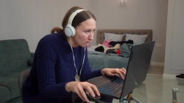 Çevrimiçi oyun oynayan, kulaklık takan, sanal dünyada gezinen, dağınık yatak odası ortamında laptop ve fare kullanan genç bir kadın.