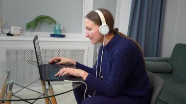 Çevrimiçi oyun oynayan, kulaklık takan, sanal dünyada gezinen, dağınık yatak odası ortamında laptop ve fare kullanan genç bir kadın.